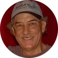 Smiling man wearing glasses and a baseball cap, a client of eMachineShop, against a red background